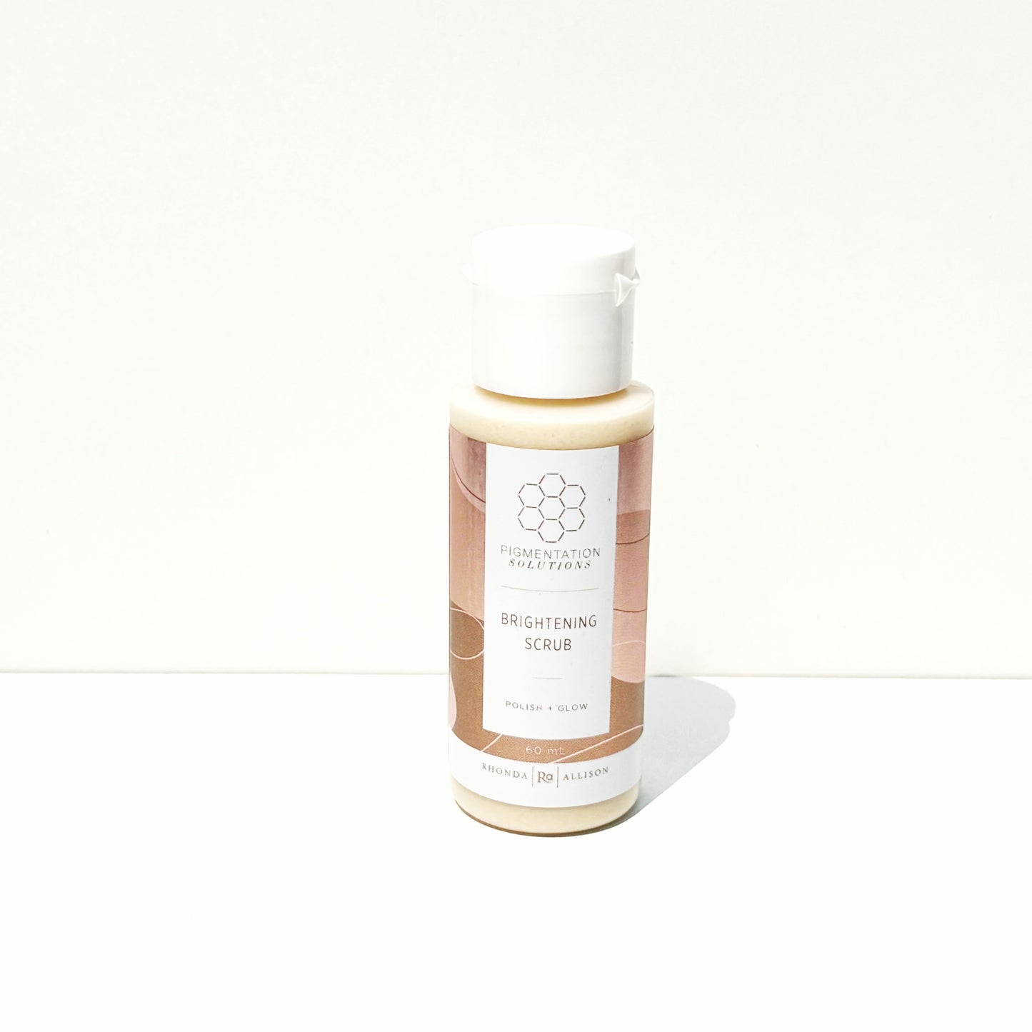 A bottle of Brightening Scrub with a white cap and a beige and brown label, set against a plain white background.