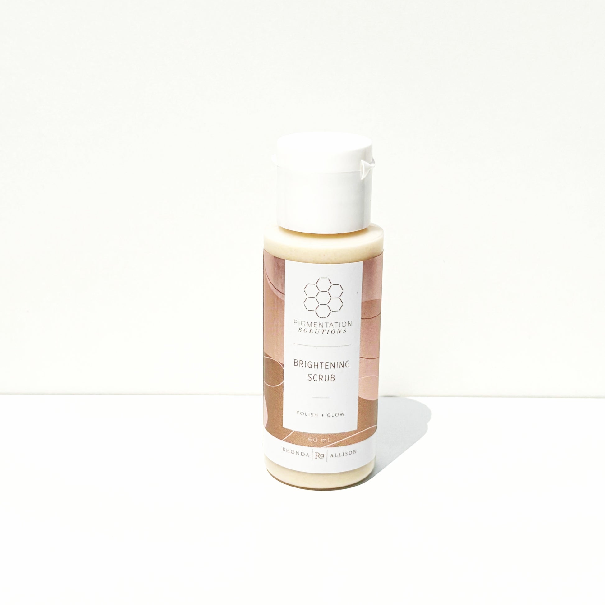 A bottle of Brightening Scrub with a white cap and a beige and brown label, set against a plain white background.